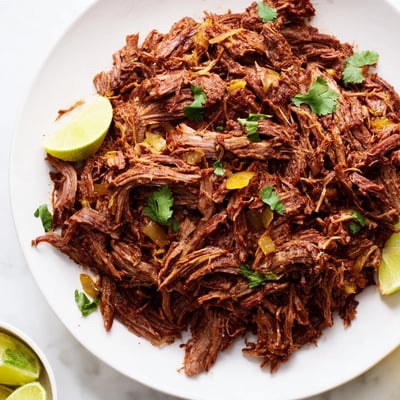 Spicy Mexican-style Slow Cooker Beef Barbacoa served in warm corn tortillas with lime wedges